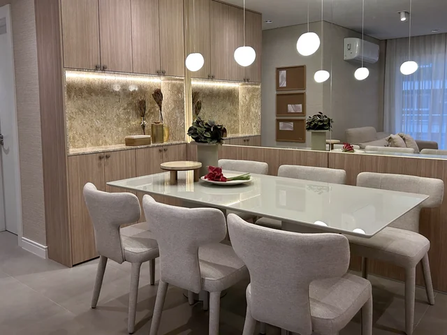 Mesa de jantar clara com cadeiras estofadas, pendentes esféricos e objetos decorativos
