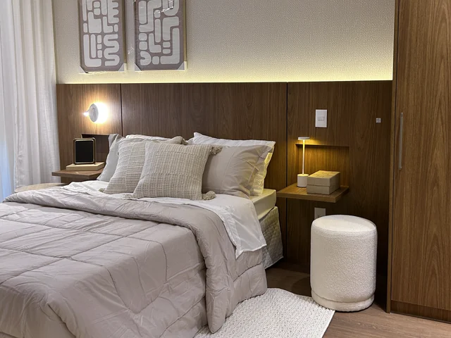 Composição de quarto com pufe claro, tapete, almofadas, quadros e iluminação de apoio