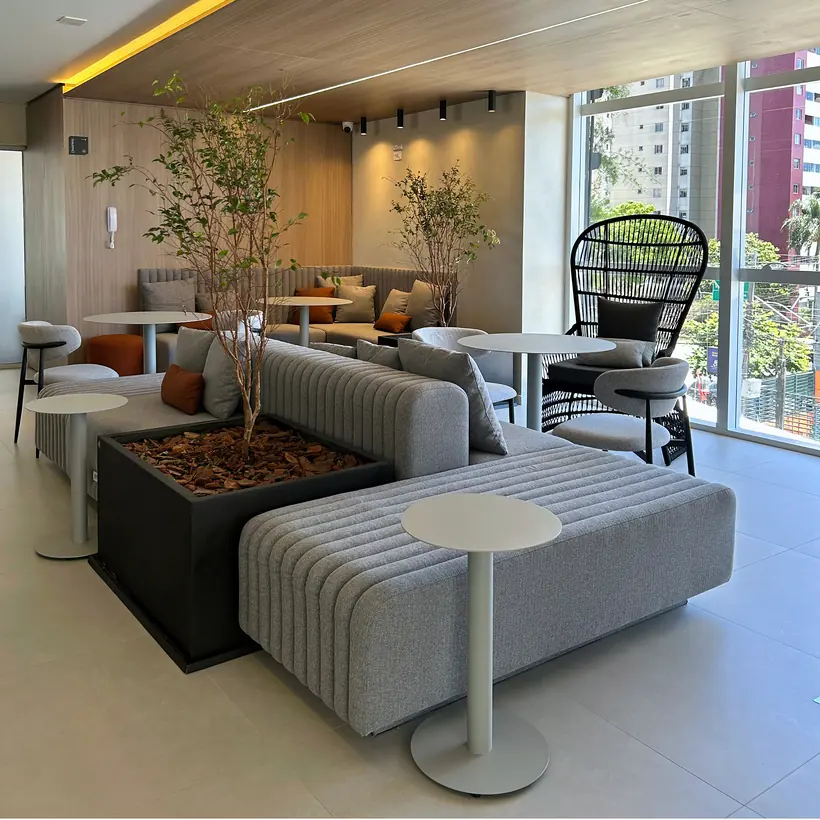 Lounge de convivência com assentos modulares, vegetação e mesas de apoio